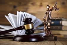 Law books lay open on a table, beside a gavel and scales of justice statue