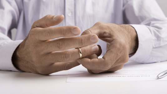 person removing wedding ring while signing divorce papers